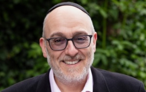 Rabbi Harvey Belovski wearing a suit with a light pink shirt and a kippah