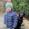 Little girl in a bobble hat and a black dog
