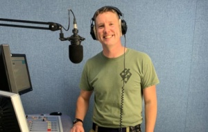 Man wearing green t-shirt and smiling casually, ready to speak into a mic
