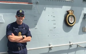 Man with arms crossed in blue navy uniform on a navy ship
