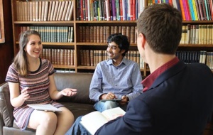 two students in a tutorial with a large shelf of books behind