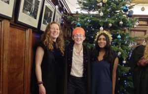A person with two friends at Christmas formal in hall, standing in front of a Christmas tree