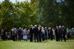 a large group pf smartly dressed people drinking and talking in a garden