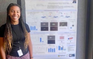 A smiling person standing in front of their poster presentation