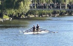 two women rowing towards a bridge with spectators