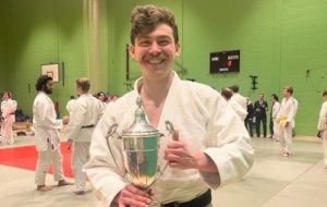 Man smiling broadly in judo uniform while holding a trophy