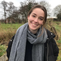 Woman smiling in field wearing grey scarf and black coat