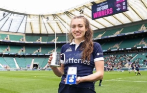 Woman in rugby kit holding tankard and medal