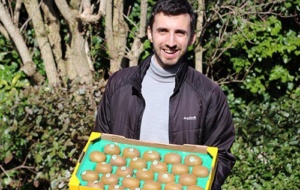 smiling man outside holding a box of kiwis