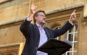 A man with glasses and a beard conducting