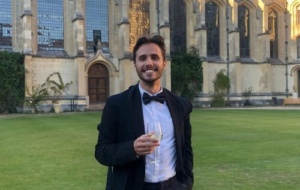 Man wearing a tuxedo holding a glass in the gardens of a college