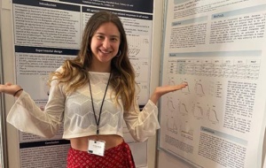 A smiling long-haired woman gesticulating dramatically at her poster presentation.