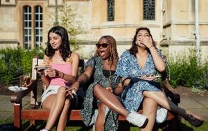 three women sitting on a bench with good and drinks, smiling and laughing animatedly