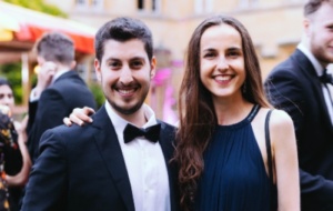 Two people in black tie at a ball smiling with arms around one another 