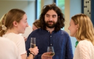 A man with a beard and long hair with two women holding glasses of wine.