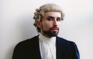 Barrister with a beard and wearing eyelliner wearing wig and traditional robes