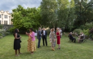 A large group of smart-casually dressed people, many holding glasses, socialising in a garden