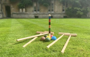 Croquet set laying on bright green grass, in the distance is an old building.