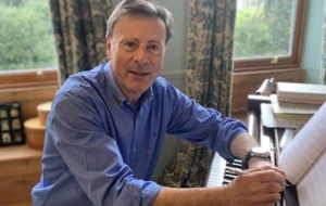 man in blue short sitting at a piano holding a pen