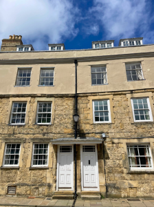 The exterior of Milne House, a large 17th century building in a mix of Cotswold stone and brown plaster.
