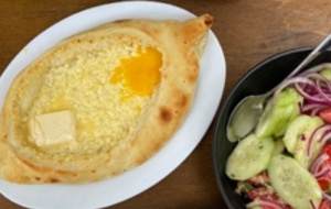 Adjaruli Khachapuri, a Georgian dish of bread filled with cheese and butter, next to a salad of cucumber, red onion and tomatoes.